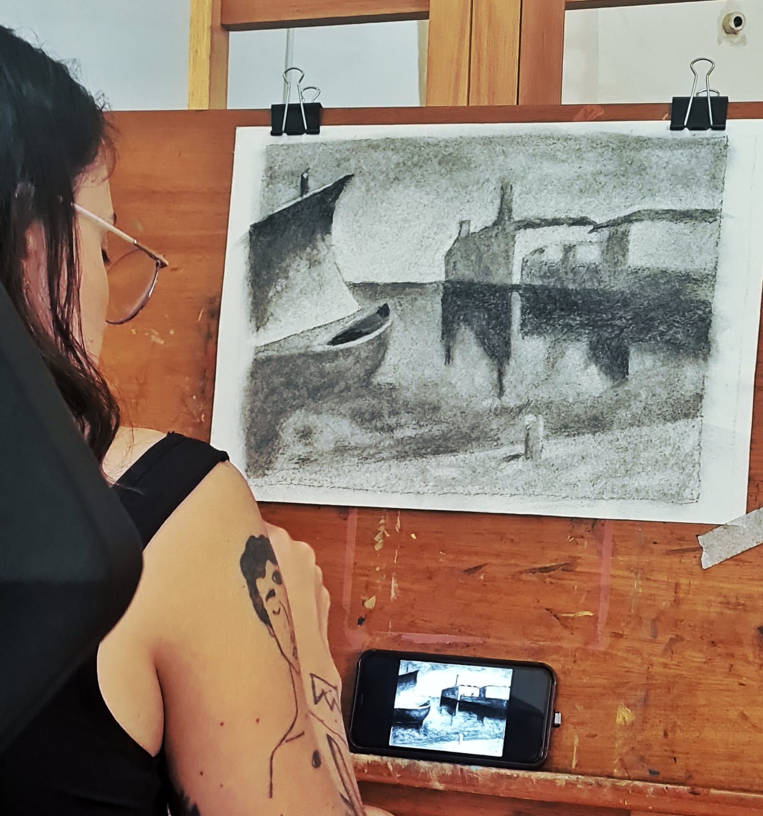 Aluna desenhando a carvão um porto com barcos e edificações no atelier de Gabriel Paz em Botafogo.
